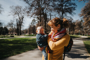 Obraz premium The image captures a cheerful moment of a happy mother embracing her baby outdoors, emphasizing love, happiness, and joy under the warm sunlight in a beautiful park environment.