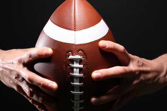 Close-up of an athlete's hand playing American football, holding a football in the air on a black background - Powered by Adobe