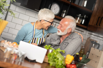 Mature couple following recipe on digital tablet while preparing lunch in the kitchen