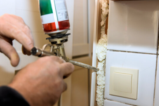 Worker uses spray sealant can to force insulating foam into crevice in wall at home improvement site.
