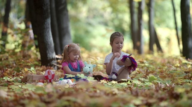 Two children happily enjoy playing with their favorite plush toys among the vibrant, colorful autumn foliage