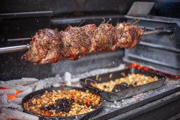 Rotisserie meat grilling over open fire with thermometer, herbs, and spices, rustic barbecue scene