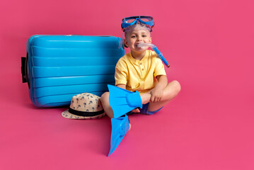 Travel, flight, vacation concept. Little cheerful boy in a swimming mask sitting in front of a blue...