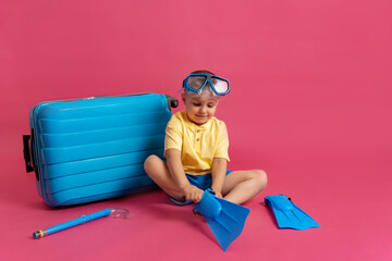 Travel, flight, vacation concept. A cheerful little boy in a blue swimming mask sits in front of a...