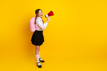 Smiling schoolgirl holds a red megaphone with excitement against a vibrant yellow background in a...