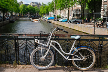 A white bicycle with a front basket parked on a bridge overlooking an Amsterdam canal