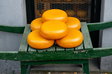 A stack of traditional Gouda cheese wheels with yellow-orange rinds, displayed on a wooden stand