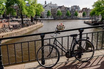 A black bicycle parked on a bridge, offering a view of an Amsterdam canal with a small boat and...