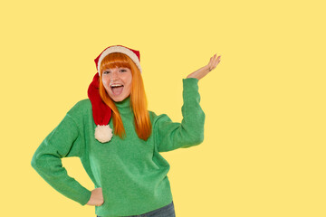 Cheerful young woman wearing a Santa hat and green sweater celebrates the holiday season with a...
