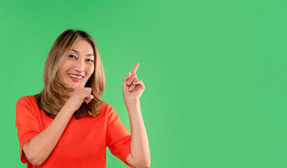 Woman in orange shirt points and smiles against a green background showcasing an enthusiastic...