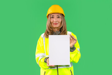 Construction worker in a bright safety jacket and helmet holds a blank white sheet on a green...