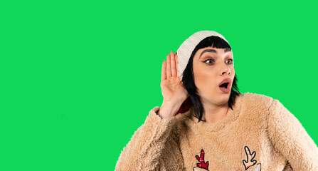 Woman with surprised expression listens intently in cozy sweater against vibrant green background