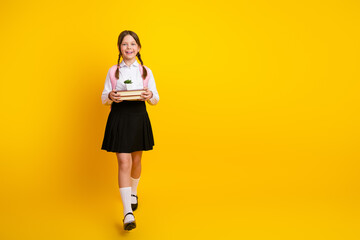 Cheerful young schoolgirl in formal uniform holding book and smiling against a vibrant yellow...