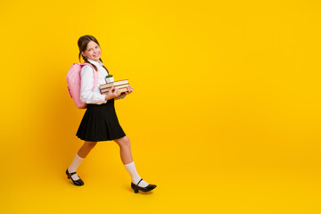 Smiling schoolgirl in a uniform holding book and a plant with a pink backpack, walking confidently...