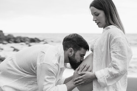 Happy couple having tender moment on the beach - Man kissing belly of pregnant woman outdoor - Family, maternity and love concept - Powered by Adobe