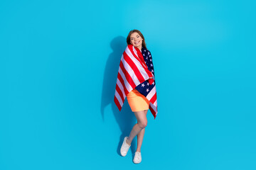 Happy young woman wrapped in American flag standing against a blue background with a bright attitude