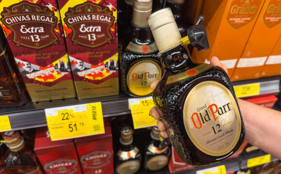 GUAYAQUIL, ECUADOR - JUN 19, 2025: Person holds Old Parr whisky bottle in supermarket shelf among other Scotch liquor brands.