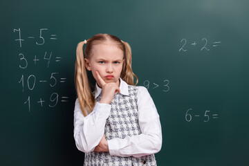 Thoughtful schoolgirl in uniform ponders math problems on chalkboard during classroom lesson in education setting
