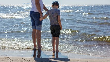 A father and his son were wading barefoot in the water by the sea. Horizontal photo.