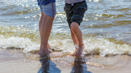 The bare feet of a father and his son in the sea water