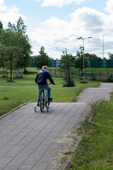 A little boy in a black jacket rides a bicycle on a mountain path in the park. View from behind