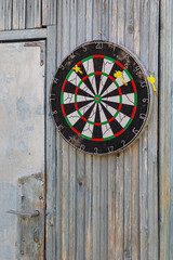A dart board is hung outdoors on an old wooden wall