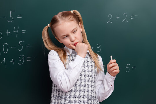 Thoughtful schoolgirl solving math equations on chalkboard in classroom during lesson focusing on problem-solving and learning