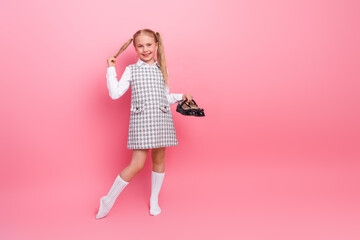 Charming little girl in stylish school uniform with ponytails posing on pink background, expresses happiness and cheerfulness