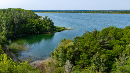 Aerial view of a scenic lakeshore with green water and dense forest surrounding a small peninsula.