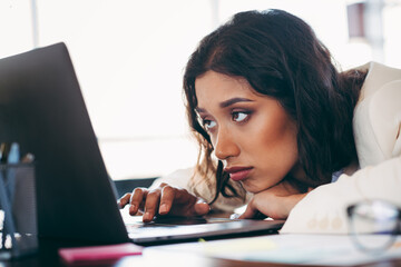 Elegant businesswoman in formal attire leaning on laptop, working in a modern office environment...