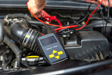 Close up mechanic using battery testing tool check up car battery in repair shop