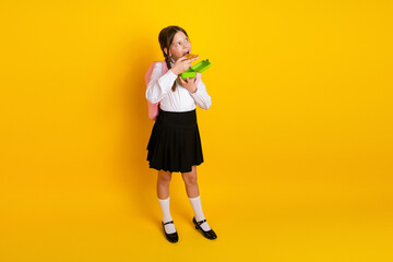 Adorable schoolgirl in uniform enjoying her meal with a lunchbox against a vibrant yellow...