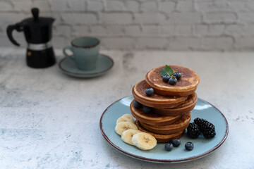 Tasty pancake stack with berries and banana slices. A moka pot and coffee cup sit nearby on the...