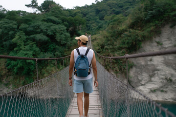 Man crosses a suspension bridge in a lush green landscape