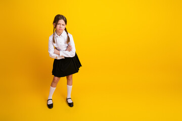 Charming young schoolgirl in formal uniform standing confidently against a vibrant yellow...