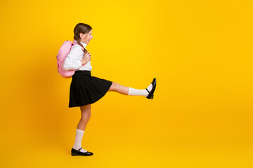 Energetic schoolgirl dressed in formal uniform with backpack posing playfully against vibrant...