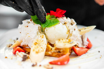 Close-up of a gourmet dessert with whipped cream, ice cream, banana, strawberries, and waffle...