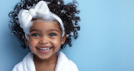 Portrait of cute smiling beautiful African American girl with blue eyes in white headband and terry robe on blue background with copy space. Happy child with curly hair, foam on head