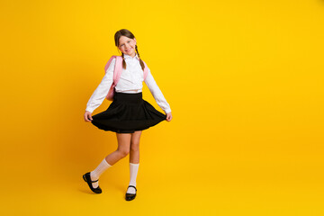 Naklejka na ściany i meble Adorable schoolgirl smiling in formal uniform against a bright yellow background, celebrating back-to-school season with joy