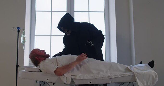 Sick man lying on couch in hospital ward, having hallucinations, seeing devil or grim reaper, being close to death, feeling like dying, staring at skeleton with terror. Death and horror concept