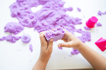 Child playing with purple kinetic sand on white surface
