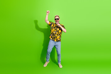 Middle aged man with beard wearing a cheerful printed shirt joyfully dancing against a solid vibrant green background