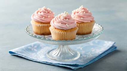 Three pink frosted cupcakes with sprinkles on a glass cake stand