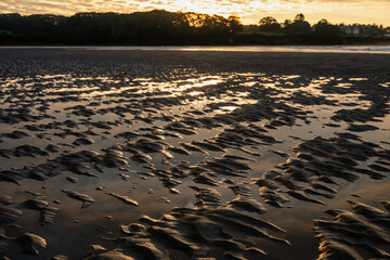 view from the shore on low tides with patterned sand in the foreground with the yellow sun rising...