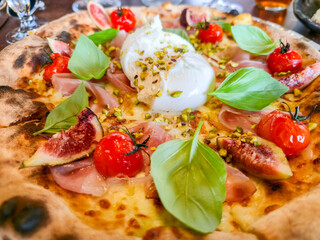 Pizza with cheese, burrata, fig, cherry tomatos, basil and ham