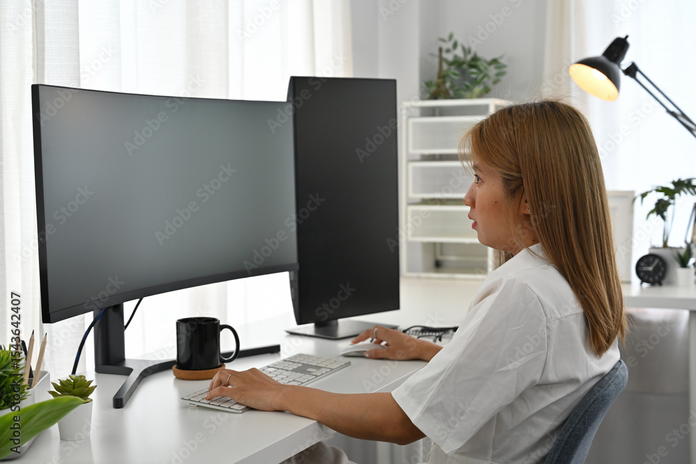 Poster focused female programmer writing code at a desk with dual monitors and a modern workspace