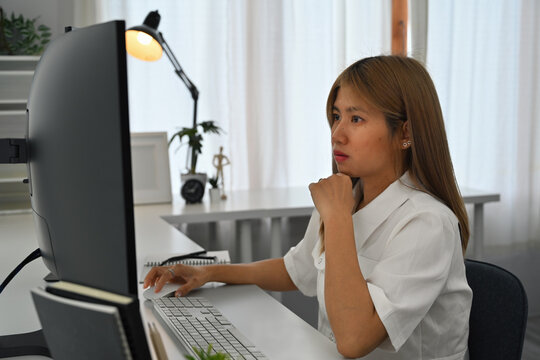 A Thoughtful female programmer concentrates on the computer while coding in a modern office setup