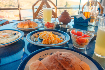 Healthy hotel breakfast with eggs, fruits, bread and juice on a sunlit table with window view. Rustic setting, travel accommodation or hospitality concept. Copacabana, Bolivia. Cozy hotel stay.