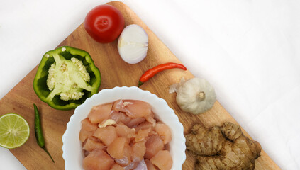 Preparation ingredients ( lime, chilies, onion, garlic, coriander root, capsicum annuum) for cooking fresh chickens on wooden cutting board, on white background.
