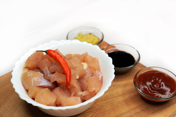 Side view of raw chicken ingredients on a wooden background. Raw chicken thighs, soy sauce, ground ginger and garlic, and other uncooked ingredients.